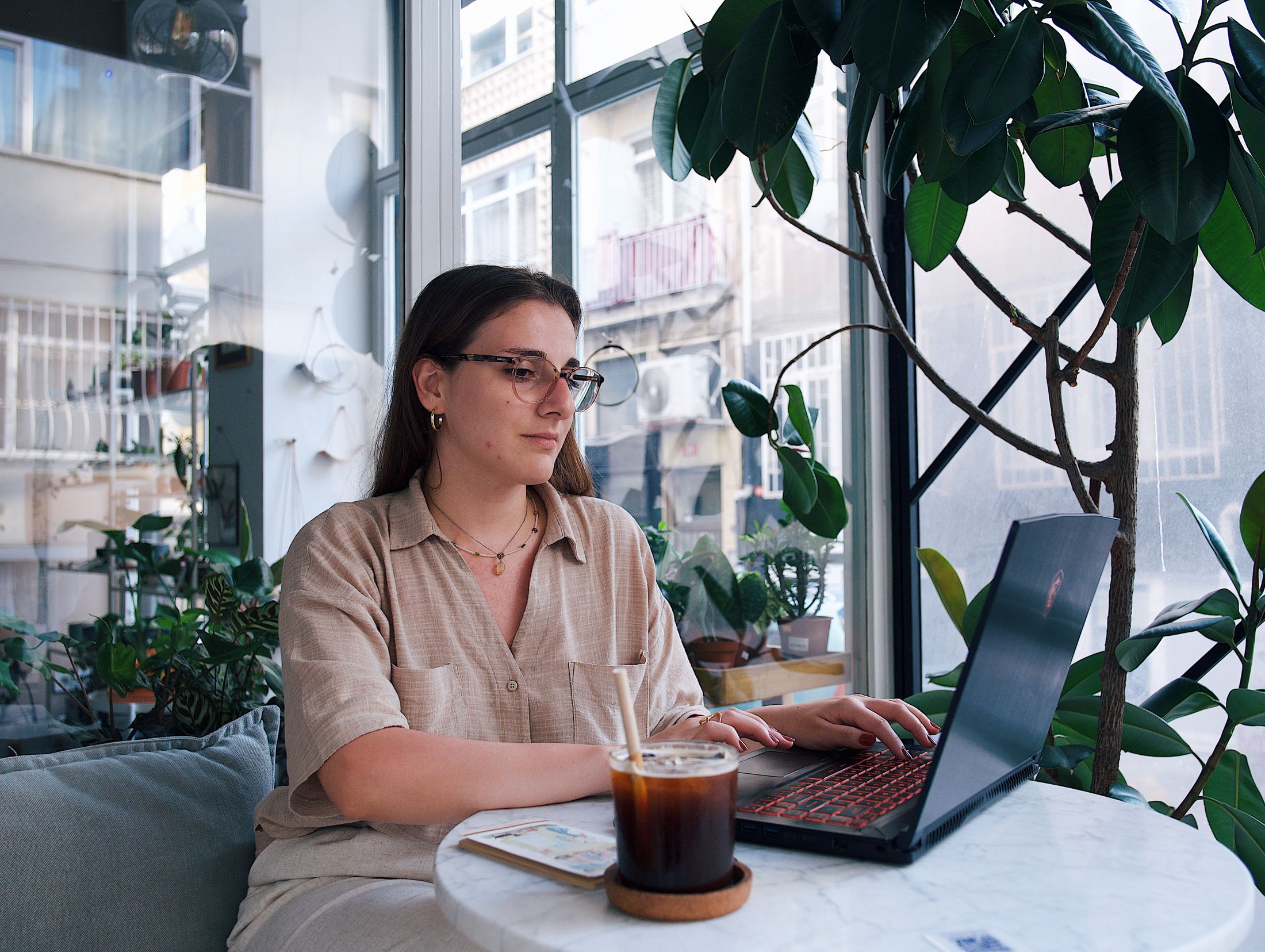 A young woman with a laptop in a plant-filled cafe