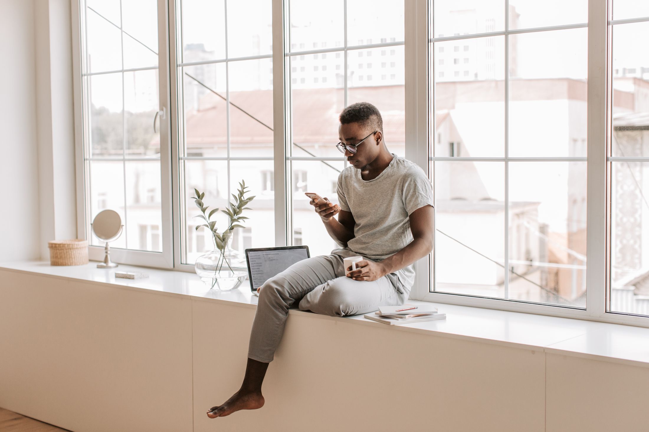 A man on a window sill reading on his smartphone